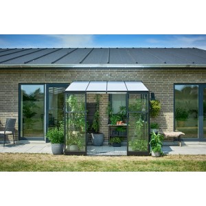 Serra da appoggio Halls Qube Lean-to 68 nera con piante e accessori da giardino contro un muro di casa.