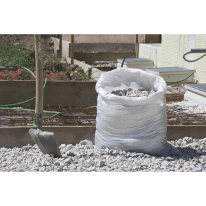 Sacco in tessuto bianco Windhager per carichi pesanti (50 kg) riempito di ghiaia, accanto a una pala.