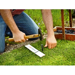 Installation du câble périphérique pour robot tondeuse Gardena avec marteau et piquet dans le jardin.