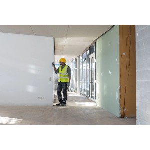 Arbeiter mit gelbem Helm misst Wand mit Bosch Laser-Entfernungsmesser GLM50-21 auf Baustelle.
