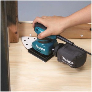Ponceuse vibrante Makita BO4565 en action sur une surface en bois.
