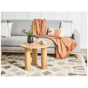 Table basse ronde marron Beliani Senoia en MDF avec trois pieds devant un canapé gris.