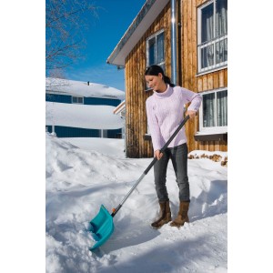 Donna che usa il manico in alluminio Gardena combisystem 130 cm con pala da neve per spalare la neve davanti a una casa.
