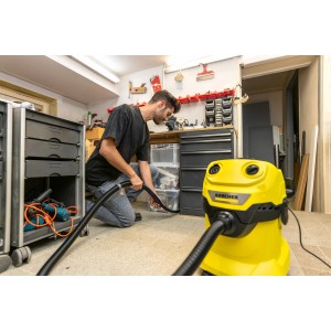 Homme utilisant un aspirateur eau et poussière Kärcher avec un suceur flexible pour le nettoyage dans un atelier.