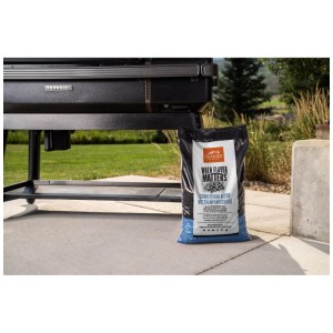 Sacco nero 9 kg Traeger Grillpellets Competition Blend Quercia Mela accanto a grill nero su patio.