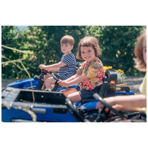 Bambini che guidano trattori blu Falk New Holland con rimorchi in giardino.