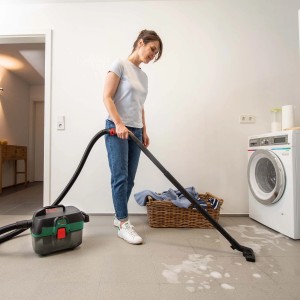 Femme aspirant du liquide avec l'aspirateur sans fil Bosch AdvancedVac 18V-8. Aspirateur eau et poussière avec accessoires.