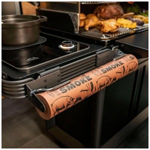 Support de rouleau Traeger P.A.L. Pop-And-Lock noir avec papier boucher marron sur un grill. Accessoire pratique.