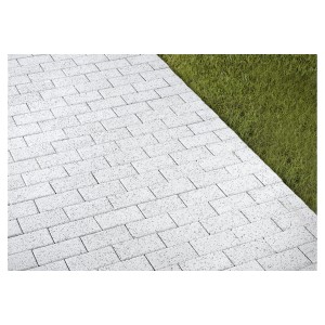 Pavés rectangulaires, lavés en blanc, posés comme allée piétonne à côté de la pelouse.