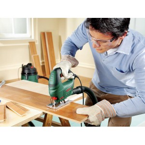 Seghetto alternativo Bosch PST 700 E in azione durante il taglio del legno. Sega verde compatta con uomo nell'immagine.