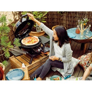 Grill a gas Outdoorchef Minichef 420 G con pizza sulla griglia, azionato da una donna in giardino.
