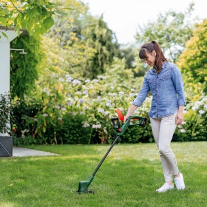 Donna taglia l'erba con il tagliabordi a batteria Bosch EasyGrassCut 18V-26 Solo in giardino.