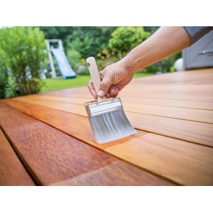 Mano che vernicia una terrazza in legno con pennello piatto LUX 100 mm. Pennello con serbatoio per grandi superfici.
