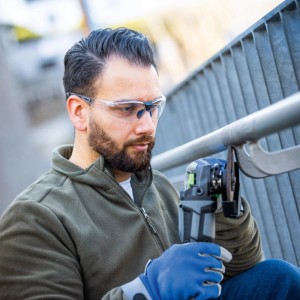 Uomo che indossa occhiali protettivi trasparenti LUX-TOOLS durante la smerigliatura del metallo.