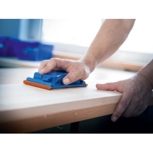 Mano che leviga il legno con il rotolo abrasivo LUX K180 e il blocco di levigatura. Abrasivi per la lavorazione del legno.