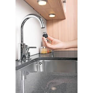 Adaptateur de robinet Kärcher pour robinets d'intérieur tenu à la main devant un robinet.