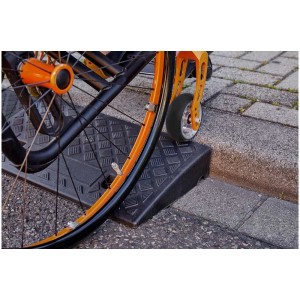 Rampa per marciapiede Cartrend (2 pz.) con sedia a rotelle che supera il marciapiede. Attrezzatura da costruzione per accesso senza barriere.
