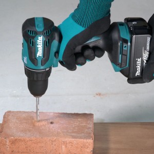 Trapano avvitatore a percussione Makita DHP490ZJ 18V turchese/nero fora un mattone rosso. Mano tiene l'utensile.
