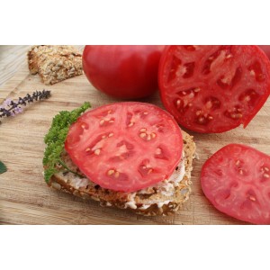 Pomodoro rosa Blu Tomate Rose Crush su pane, affettato e intero su tagliere di legno.