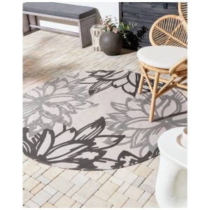 Runder Outdoor-Teppich Solapur mit floralem Grau-Beige-Muster auf heller Terrasse.