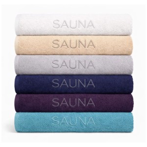 Serviettes de sauna empilées en blanc, beige, gris, bleu, violet et turquoise avec inscription.