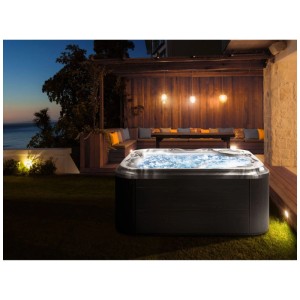 Spa extérieur Beliani Tularosa gris graphite avec eau bouillonnante LED dans un jardin la nuit.