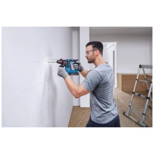 Uomo che fora un muro con un trapano a percussione a batteria Bosch Professional GBH 18V-18 blu.