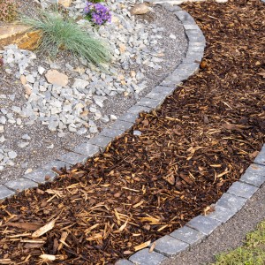 Sentiero di pacciame di corteccia in giardino, delimitato da pietre. Pacciame di corteccia naturale per aiuole.