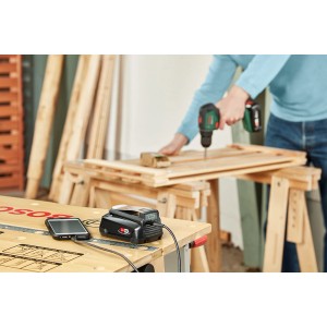 Bosch Adattatore USB per batteria Powerbank 18V-45 con smartphone in carica, avvitatore a batteria in uso sullo sfondo.