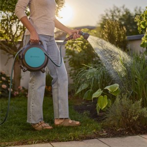 Donna che innaffia il giardino con Gardena Schlauchbox Move 10 m. Carrello avvolgitubo mobile con spruzzatore.