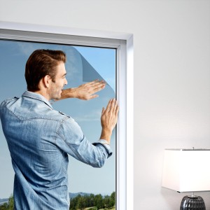Un homme installe un kit de protection anti-pollen anthracite Windhager sur une fenêtre.