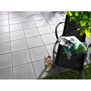 Pietre per terrazza Kann Sincera grigie 40x40 cm posate con sedia, coperta e scarpe sulla terrazza.