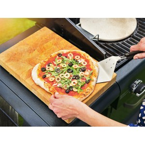 Pelle à pizza avec pizza sur planche à découper en bois à côté du barbecue. Surface de 24 cm.