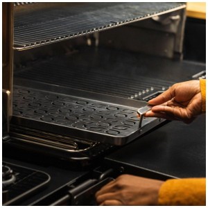 Mano inserisce teglia grill Traeger ModiFIRE® in acciaio inox per pesce e verdure nel barbecue.