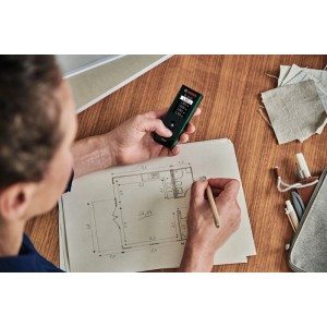Person misst mit Bosch Laser-Entfernungsmesser Zamo und zeichnet Grundriss. Präzises Messwerkzeug für Planung.