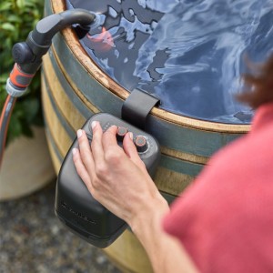 Gardena Pompe de récupération d'eau de pluie 2400 ComfortAutomatic sur cuve avec main sur les commandes.