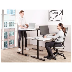 Elektrisch höhenverstellbarer Beliani Schreibtisch Destinas Weiss-Schwarz im modernen Büro. Eine Person steht, eine sitzt am Bürotisch.