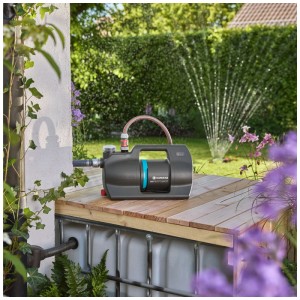 Pompe de jardin Gardena 5000 Silent en utilisation : Pompe grise avec détail bleu sur bois, arroseur en arrière-plan.