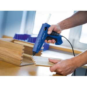 Applicazione di una pistola per colla a caldo LUX blu con stick di colla a caldo trasparenti per incollare il legno.
