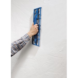 Rabot à plâtre LUX 50 cm en utilisation : main rabotant du plâtre sur un mur blanc. Idéal pour les travaux de placo.
