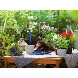 Nappe de protection grise sur table en bois dans le jardin, pour rempoter des plantes avec terreau et outils.