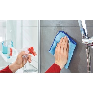 Nettoyage de carreaux avec un vaporisateur et un chiffon bleu dans la salle de bain.