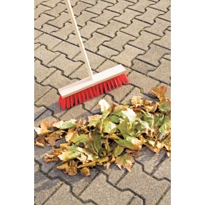 Balai de voirie LUX 40 cm avec manche et poils rouges balayant des feuilles sur des pavés.