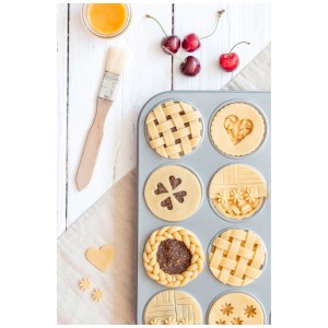 Backpinsel aus Naturmaterial neben Mini-Tartelettes in Backform und Kirschen.