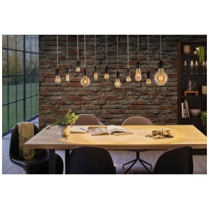 Dekorative Paulmann LED Vintage-Kerze E14 Goldlicht über Esstisch mit Ziegelwand im Hintergrund.