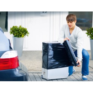 Homme emballant une valise avec du film étirable noir LUX pour déménagement ou transport.