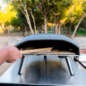 Spazzola per forno pizza Ooni in uso per pulire un forno per pizza. Utensile per barbecue con manico in legno.