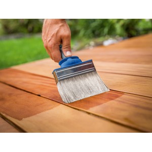 Mano che tinge il legno con pennello piatto LUX 120 mm. Pennello con serbatoio per impregnante.