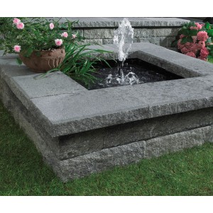 Mur en pierre brute avec plaque de recouvrement nuancée de gris et petite fontaine dans le jardin.