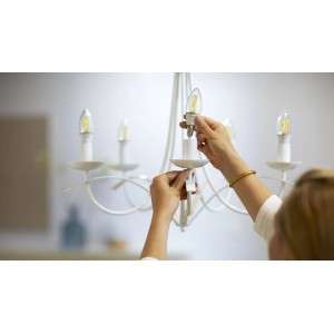 Donna avvita lampadina a filamento LED Smart Philips in un lampadario.